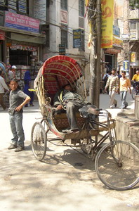 Deze riksja-rijder rust uit van zijn arbeid, terwijl het verkeer om hem heen gewoon doorgaat (o.a. met toeteren).